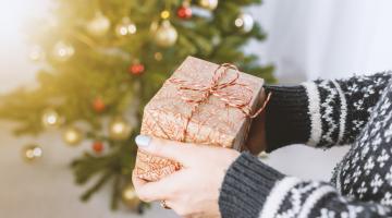 a lady is holding a christmas present in front of a christmas tree during the holiday season