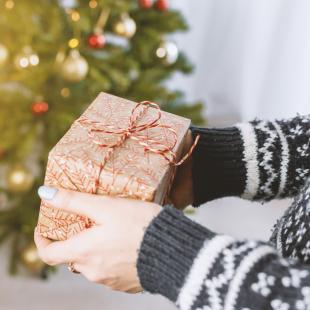 a lady is holding a christmas present in front of a christmas tree during the holiday season