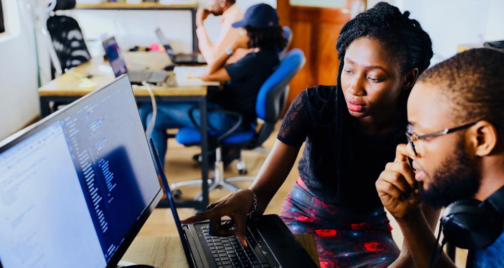 a guy and a girl sit at a computer reading something