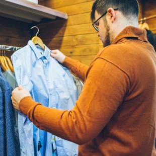 a guy contemplates whether he should purchase the light blue shirt or medium blue shirt
