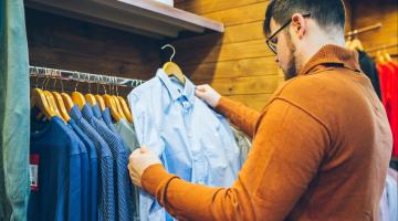 a guy contemplates whether he should purchase the light blue shirt or medium blue shirt