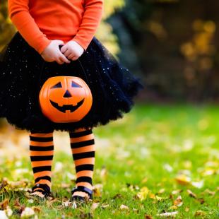 Little girl in Halloween costume and candy bucket playing in park