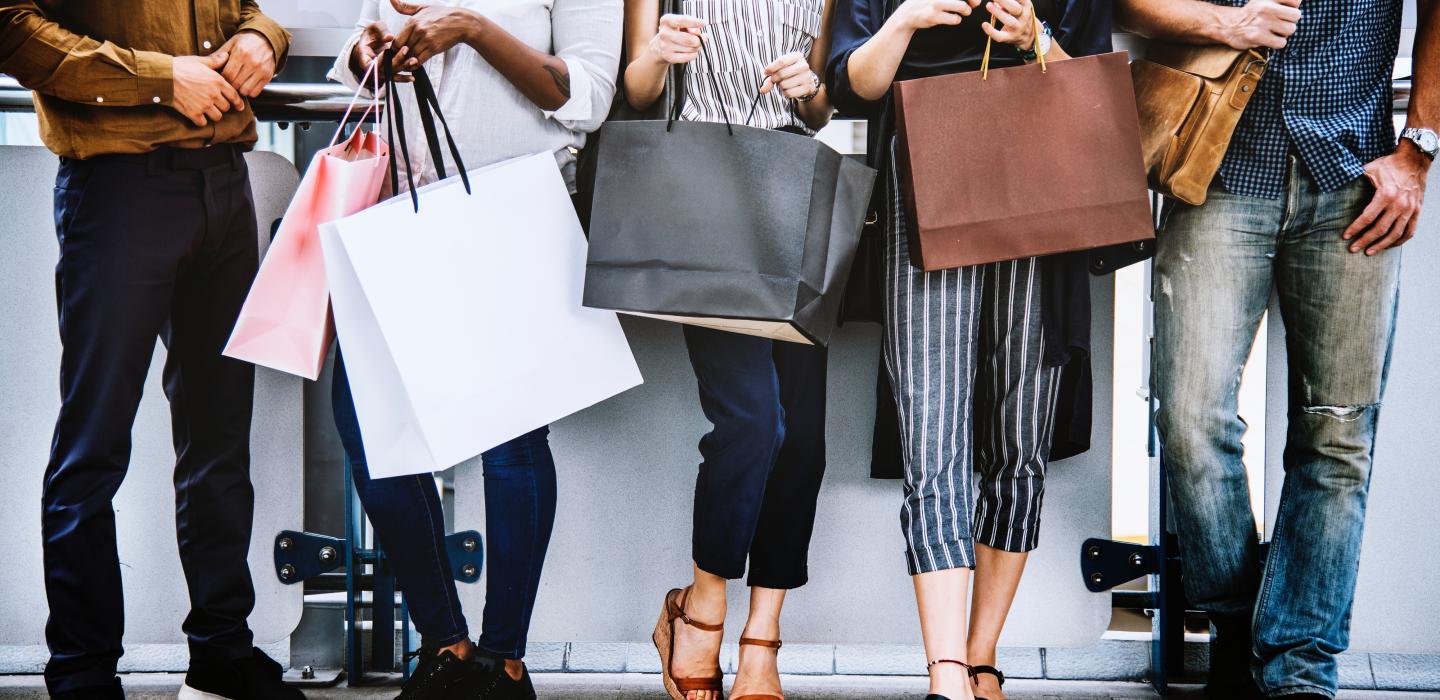 Men and women leaning against wall talking and holding shopping bags
