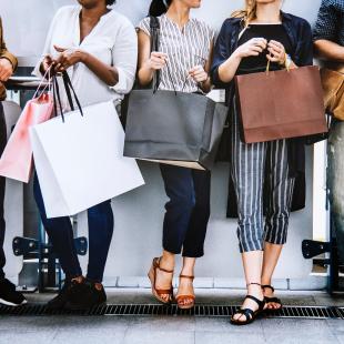 Men and women leaning against wall talking and holding shopping bags