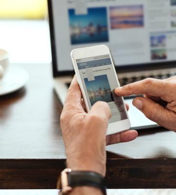 Two hands holding and swiping phone with computer in background