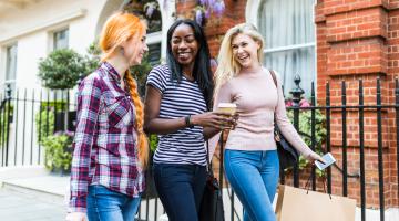 Three women laughing and walking with shopping bags