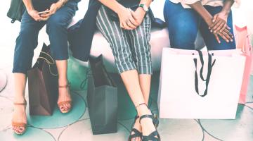 three women sit on a bench with their shopping bags