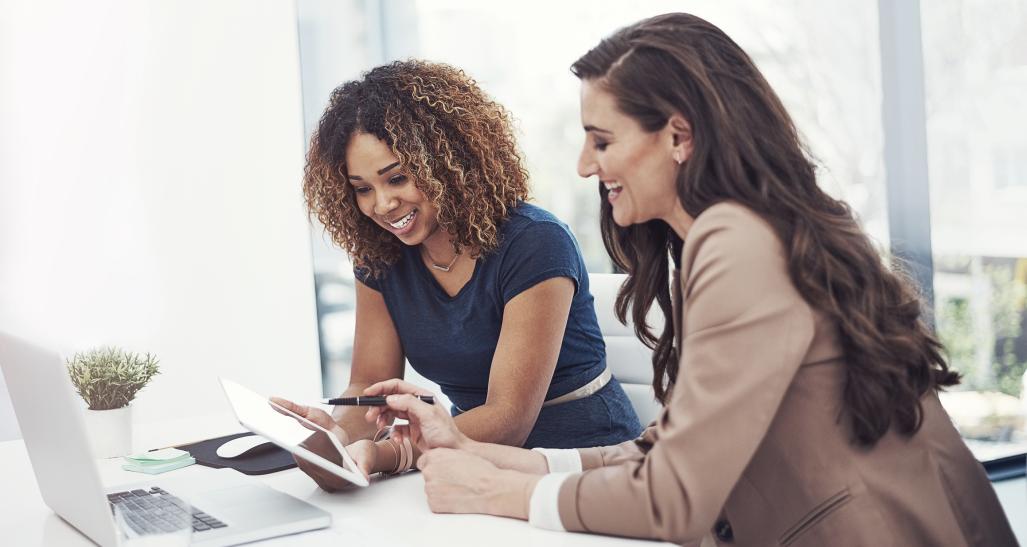 two women are smiling while at work on their computers
