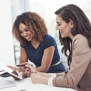 two women are smiling while at work on their computers