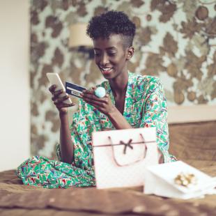 woman is sitting on her bed with her phone and credit card in hand getting ready to order something offline