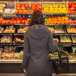woman pondering choosing produce at a grocery store